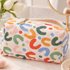 A quilted cosmetic pouch with a colorful abstract print, styled on a marble surface next to a mirror and tulips.