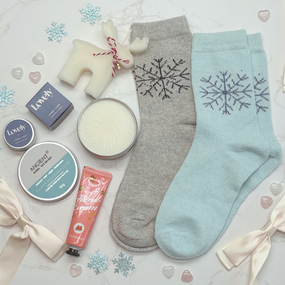 Two pairs of socks with snowflake designs, a candle, and skin care products on a festive background.