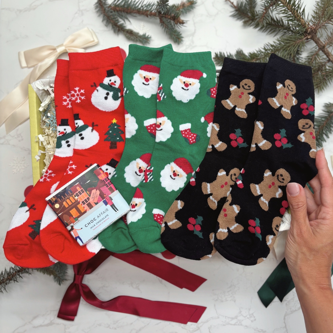 Set of Christmas-themed socks with a hand holding a card against a snowy background.