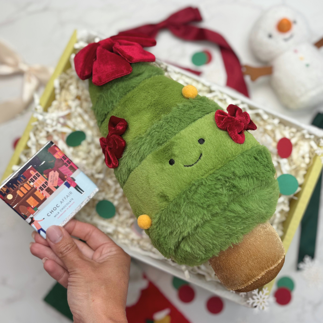 Green plush toy with a red bow held by a hand against a festive background.